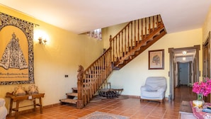 A spacious living room with a wooden staircase, a large framed artwork, a chair, and a small table with decorative items. - Amazing home in Lucena (Lucena)