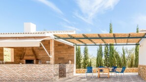 An outdoor patio with a stone fireplace, wooden pergola, and blue chairs. - Amazing home in Lucena (Lucena)