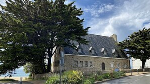 A stone building with a sloped roof, surrounded by trees and a clear sky. - Studio in a magnificent villa with private beach access. (Esquibien)