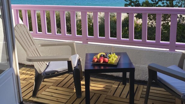 A balcony with a table set with fruit, a chair, and a sofa. - Studio in a magnificent villa with private beach access. (Esquibien)