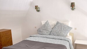 A bedroom with a bed, a wooden dresser, and two wall-mounted lamps. - Studio in a magnificent villa with private beach access. (Esquibien)