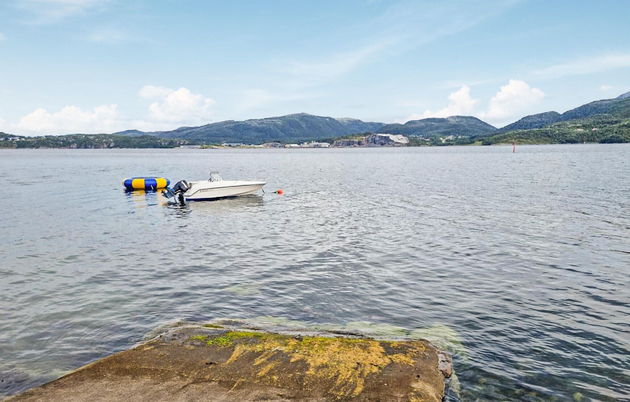 A calm lake with a small boat anchored near a dock, surrounded by mountains and clear skies.