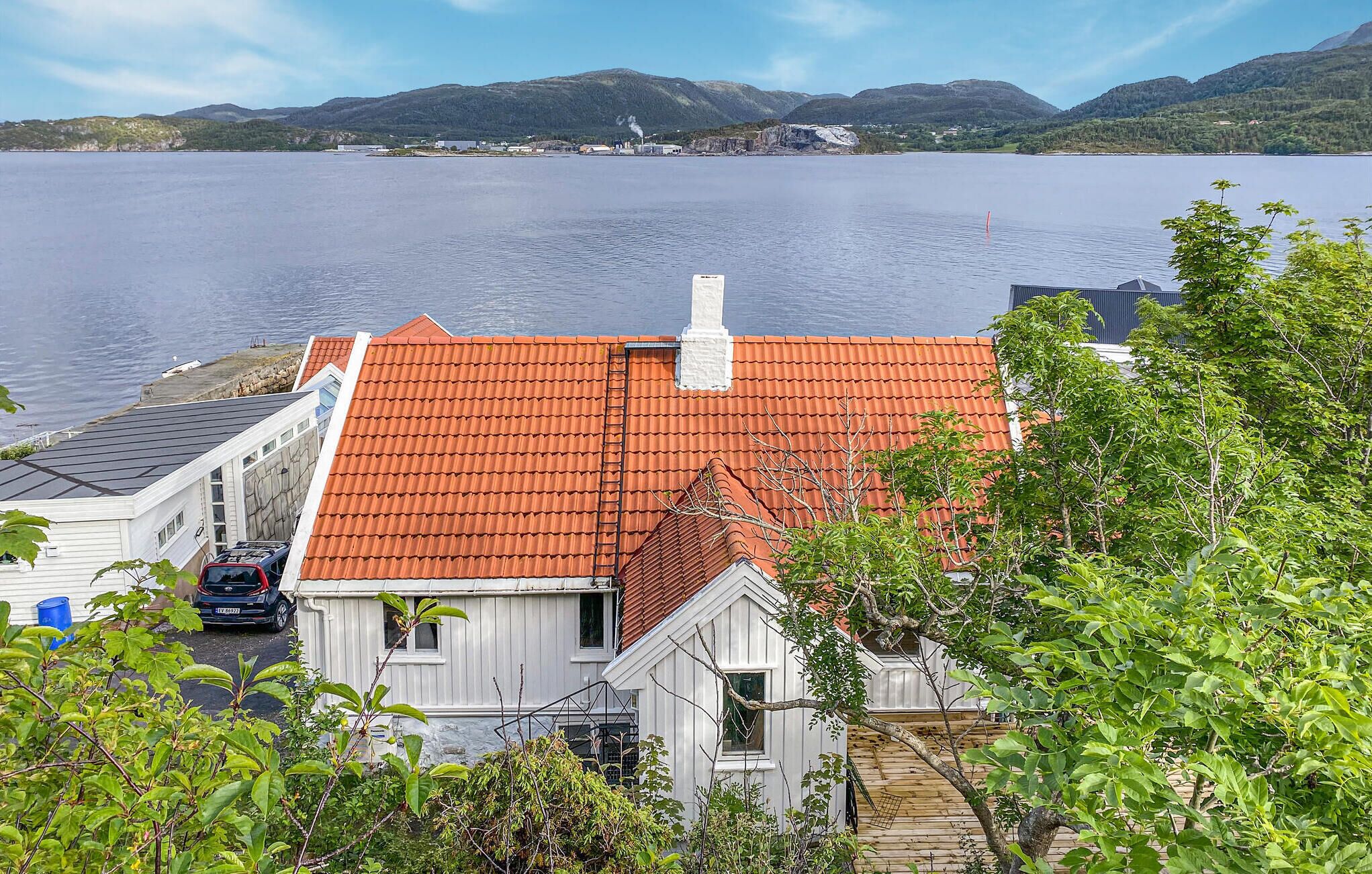 Une maison avec un toit recouvert de tuiles rouges, surplombant un lac et entourée de verdure.