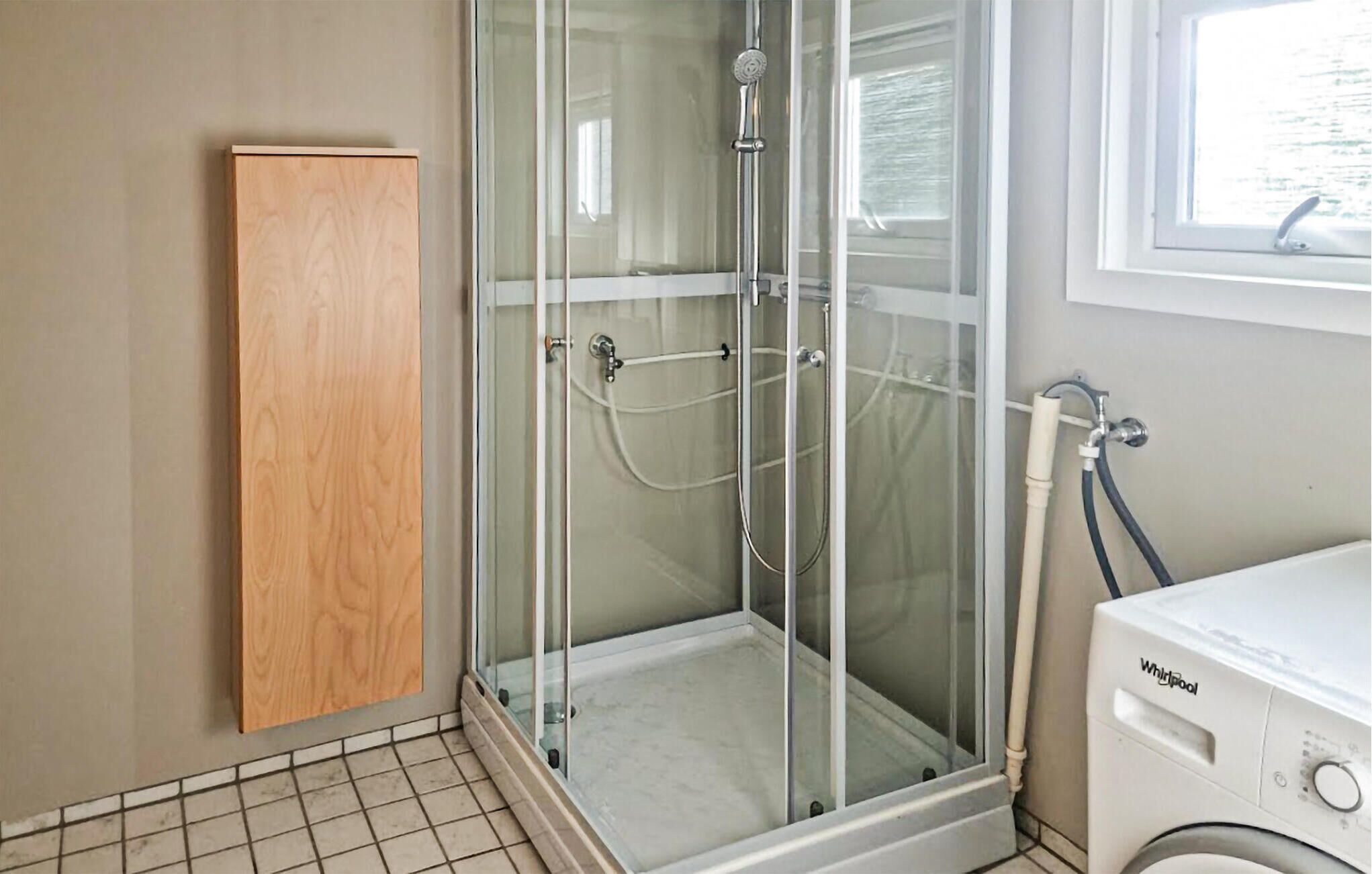 A bathroom with a glass shower enclosure, a wooden cabinet, and a washing machine.