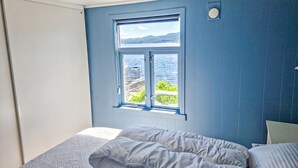 Een slaapkamer met een groot raam met uitzicht op water en groen.