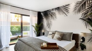 Quarto moderno com uma cama grande, vista para o verde lá fora e decoração de parede com tema tropical.