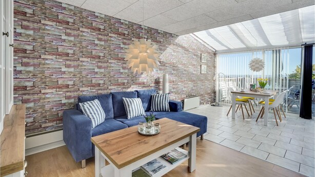 A modern living room with a blue sofa, wooden coffee table, and a brick-patterned wall. - Cozy apartment in Rømø with kitchen (Rømø)