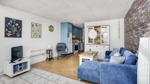 A modern living room with a blue sofa, a TV stand, and a kitchen area with blue cabinets and a white countertop. - Cozy apartment in Rømø with kitchen (Rømø)