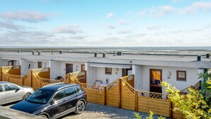 A row of white buildings with numbered doors, a parking area with cars, and a view of the sea. - Cozy apartment in Rømø with kitchen (Rømø)