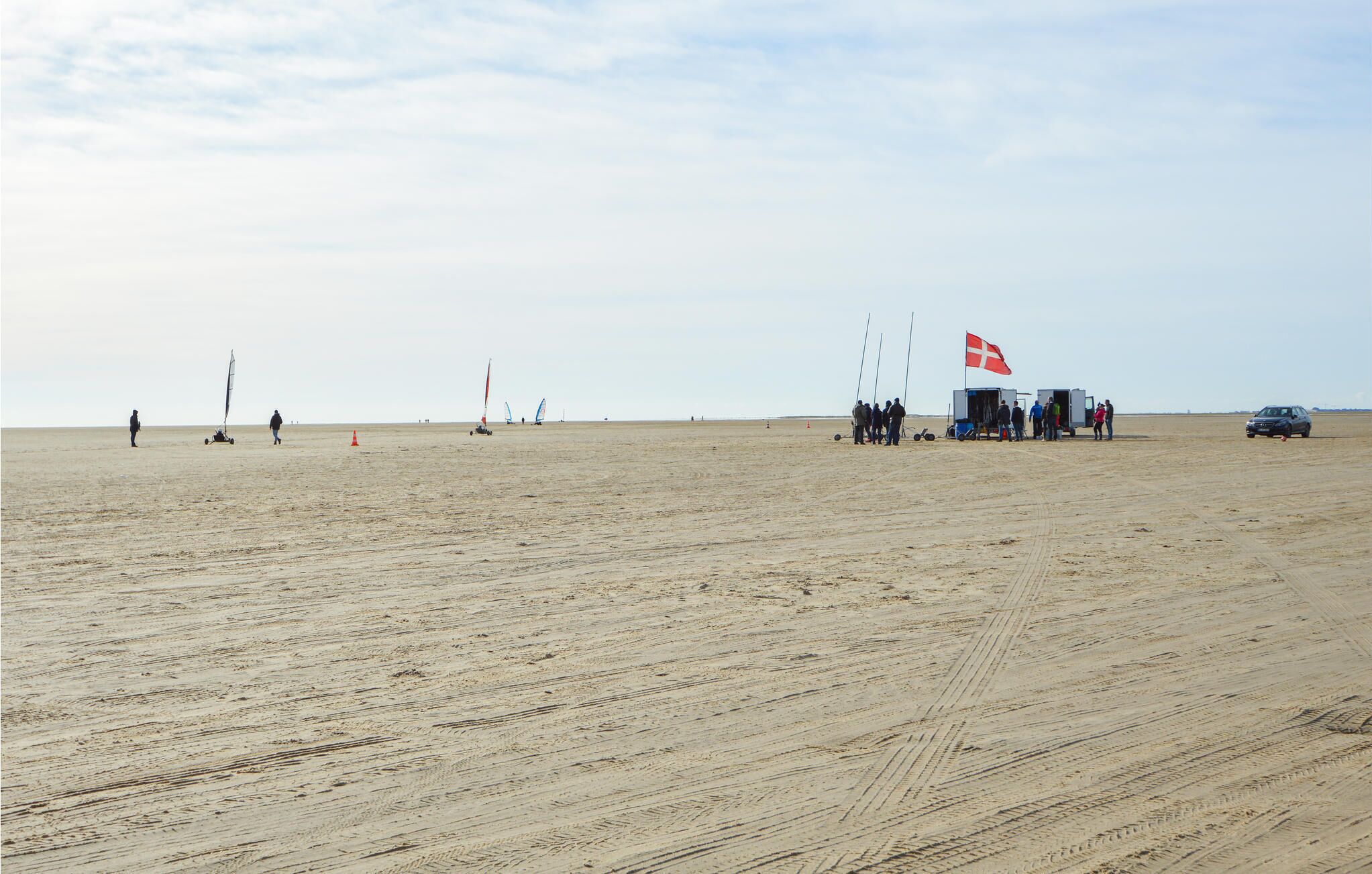 Uma extensa praia de areia aberta com algumas pessoas e equipamentos de windsurf.