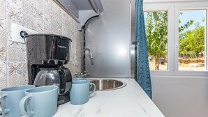 A kitchen with a coffee maker, two mugs, a sink, and a window with a view of trees. - Nice apartment in Danilo with WiFi (Danilo)