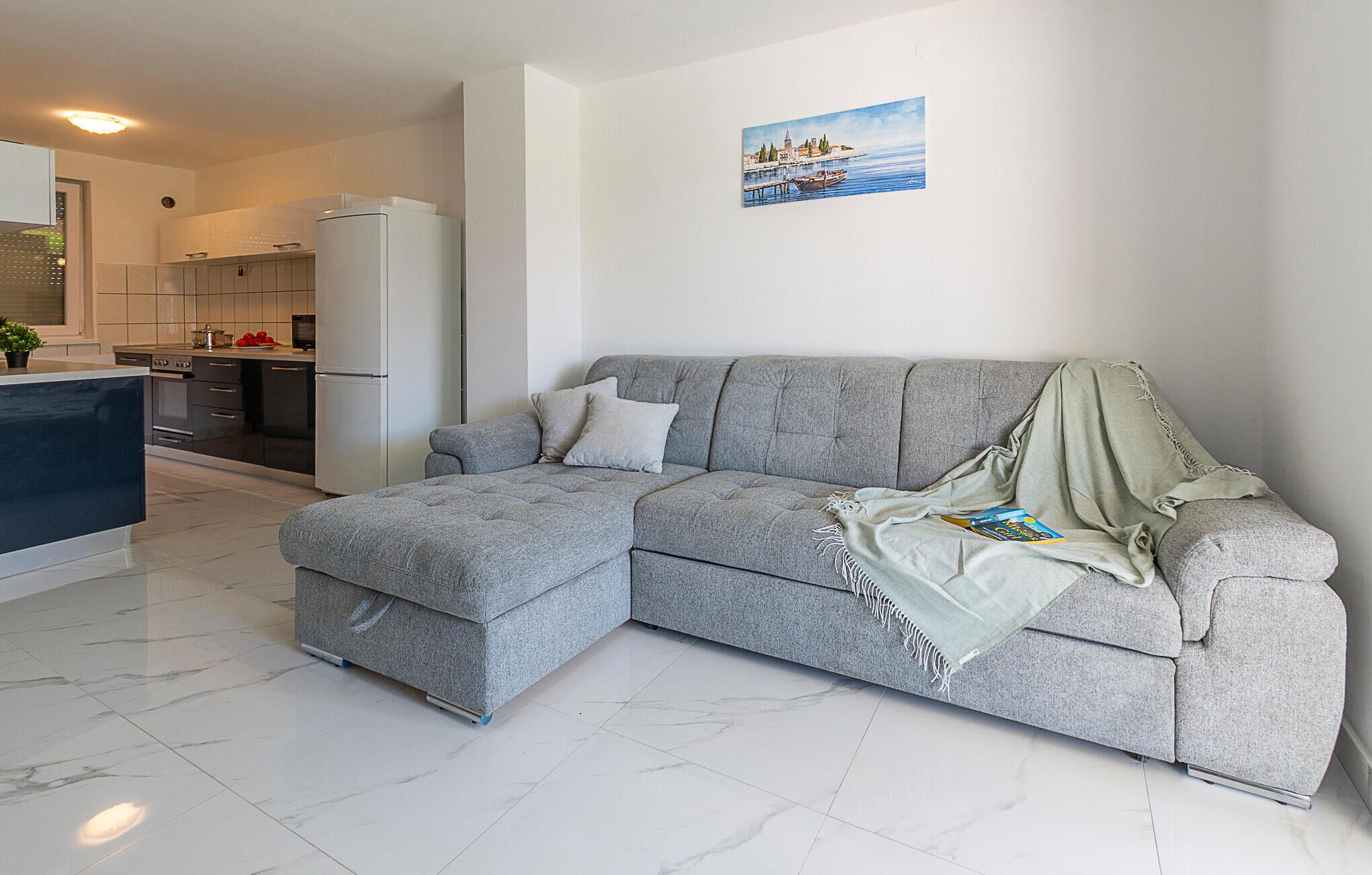 Una sala de estar moderna con un sofá seccional gris, una pequeña cocina y un cuadro en la pared.
