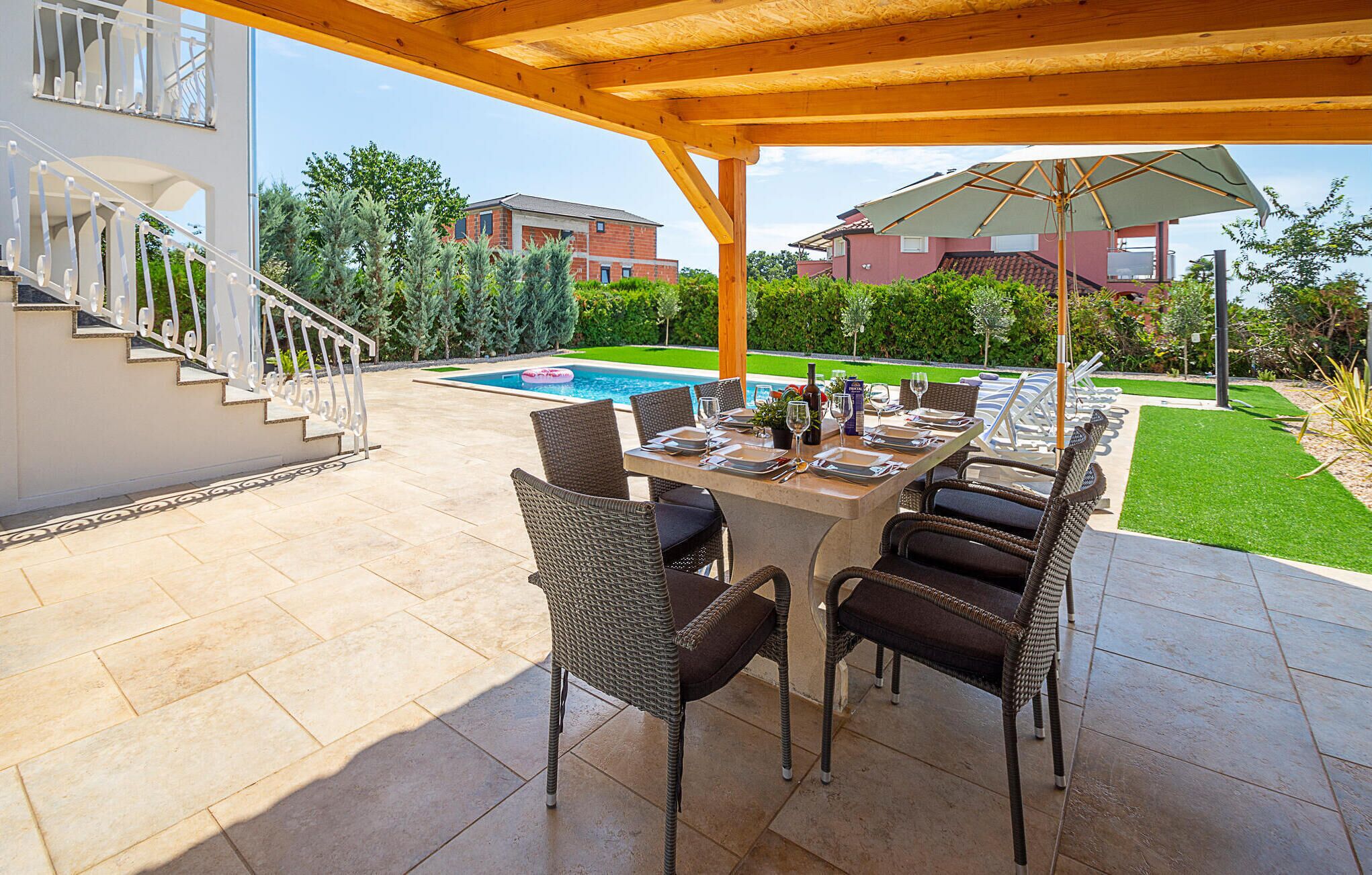 A covered outdoor dining area with a pool in the background.