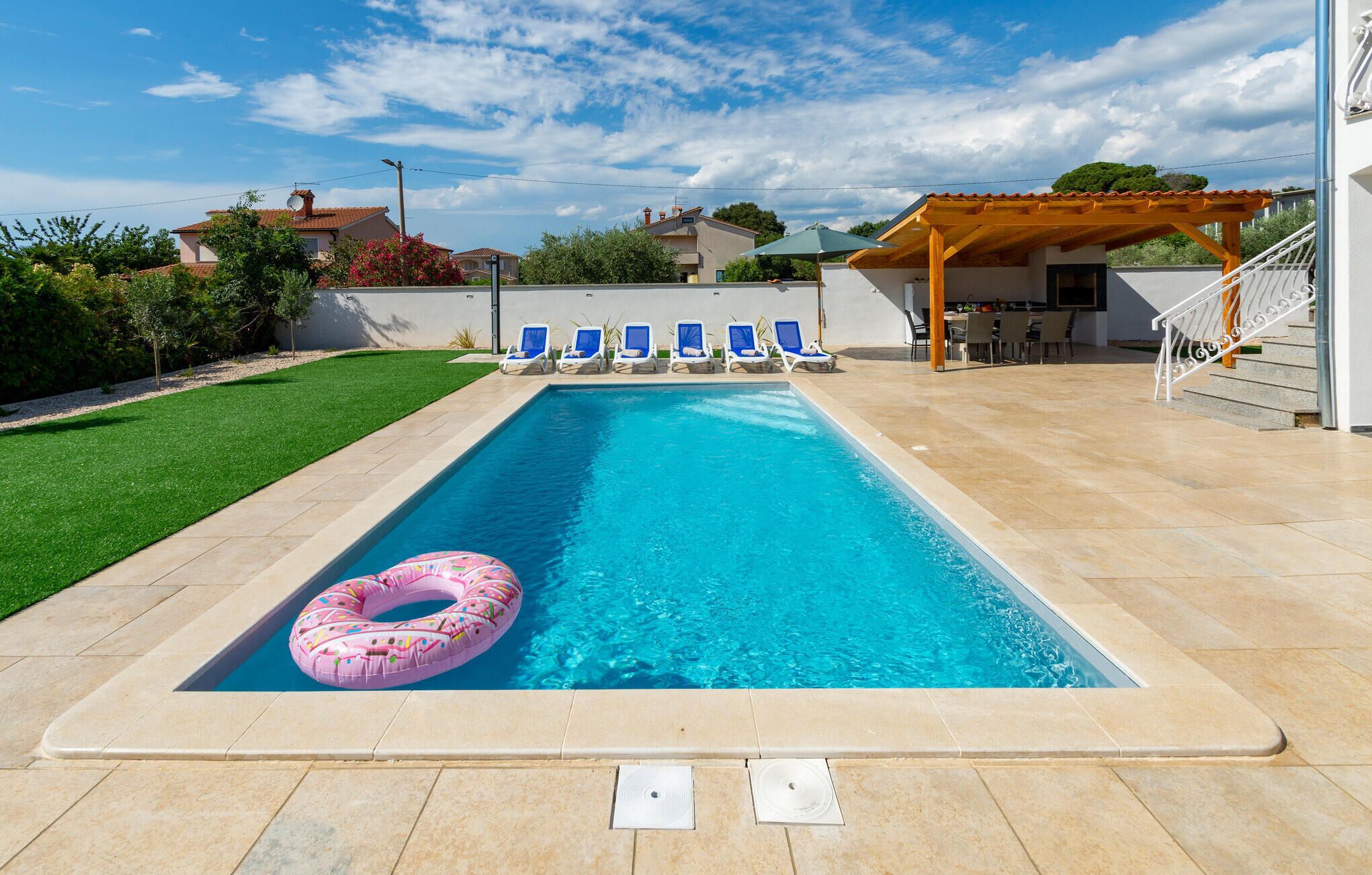 Ein rechteckiger Swimmingpool mit einem rosa Schwimmreifen, umgeben von einer gefliesten Terrasse.