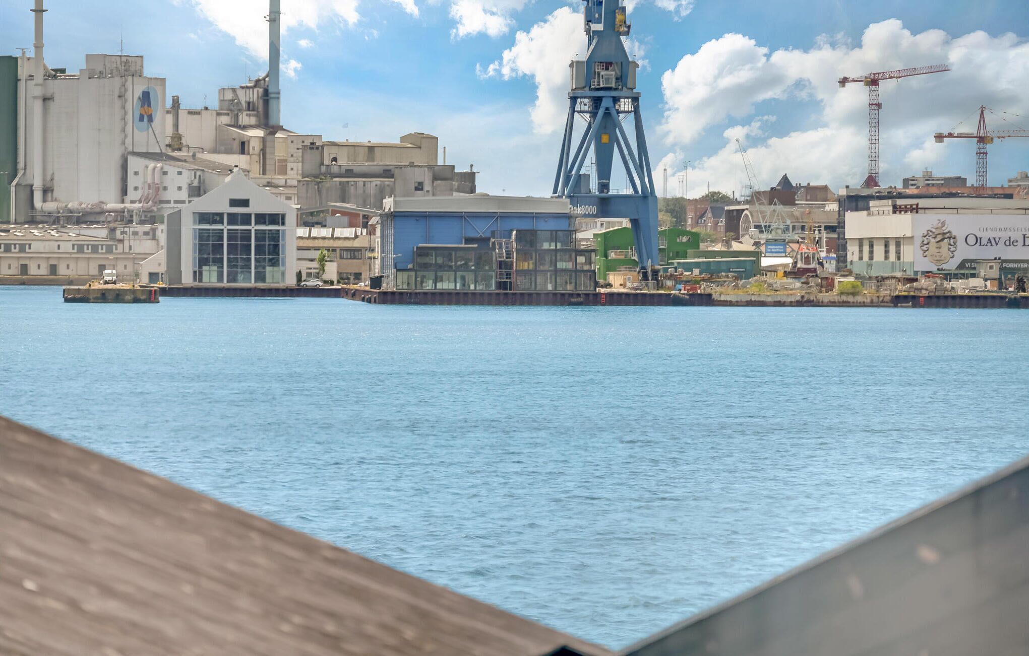 Une zone industrielle située au bord de l’eau, avec de grands bâtiments, une grue et un quai où est amarré un bateau.