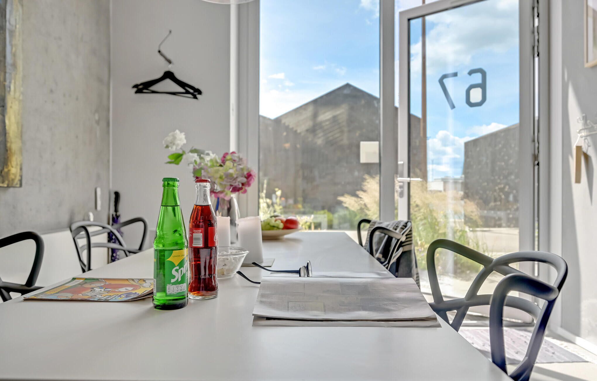 A dining table with chairs, a bottle of Sprite, a bottle of red drink, a bowl of fruit, and a newspaper.