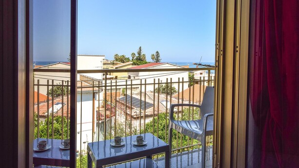 A balcony with a table and chairs, overlooking a residential area with houses and a clear sky. - Gorgeous apartment in Marina di Caronia with WiFi (Marina di Caronia)