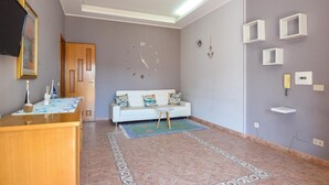A living room with a white sofa, a wooden cabinet, a clock, and a tiled floor. - Gorgeous apartment in Marina di Caronia with WiFi (Marina di Caronia)