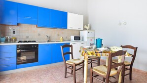 A compact kitchen with blue cabinets, a white microwave, and a dining table with chairs. - Gorgeous apartment in Marina di Caronia with WiFi (Marina di Caronia)