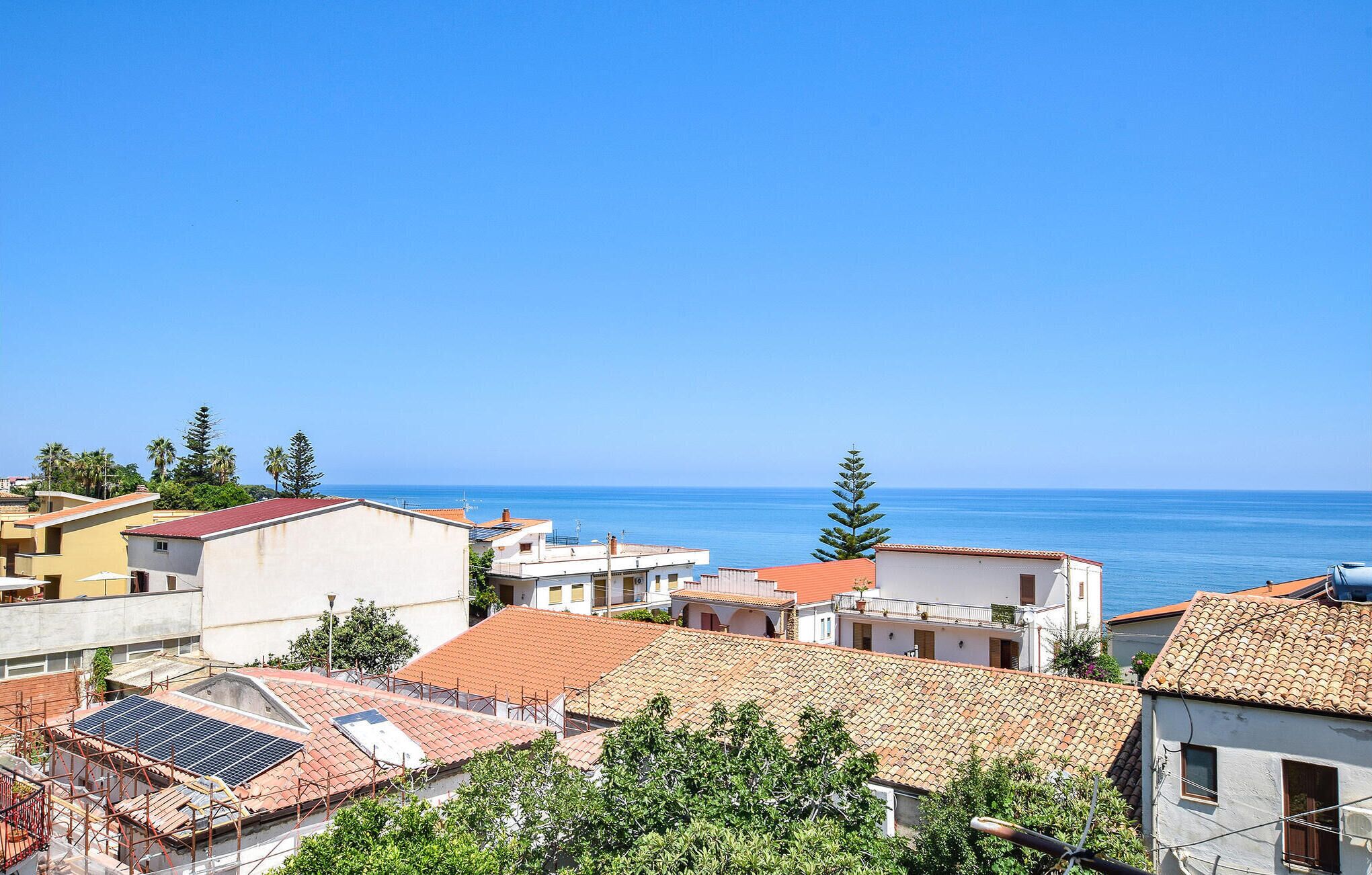 A coastal town with buildings, some with red-tiled roofs, and a clear view of the sea.