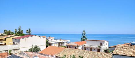 A coastal town with buildings, some with red-tiled roofs, and a clear view of the sea.