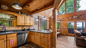 A spacious kitchen with wooden cabinets, a dishwasher, and a large island. There are multiple windows providing natural light and views of the outdoors. - Sunset Mountain Views • 3 King Suites • Hot Tub • Game Room • 8 mi to Dollywood (Sevierville)