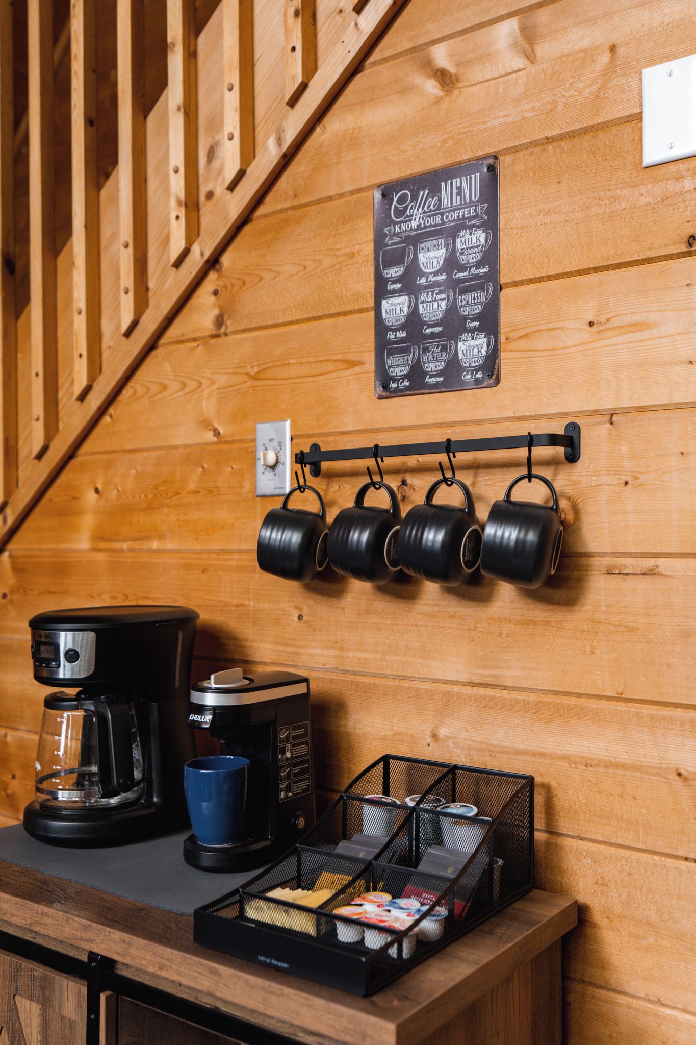 A wooden interior with a coffee station featuring a coffee maker, kettles, and a menu sign.