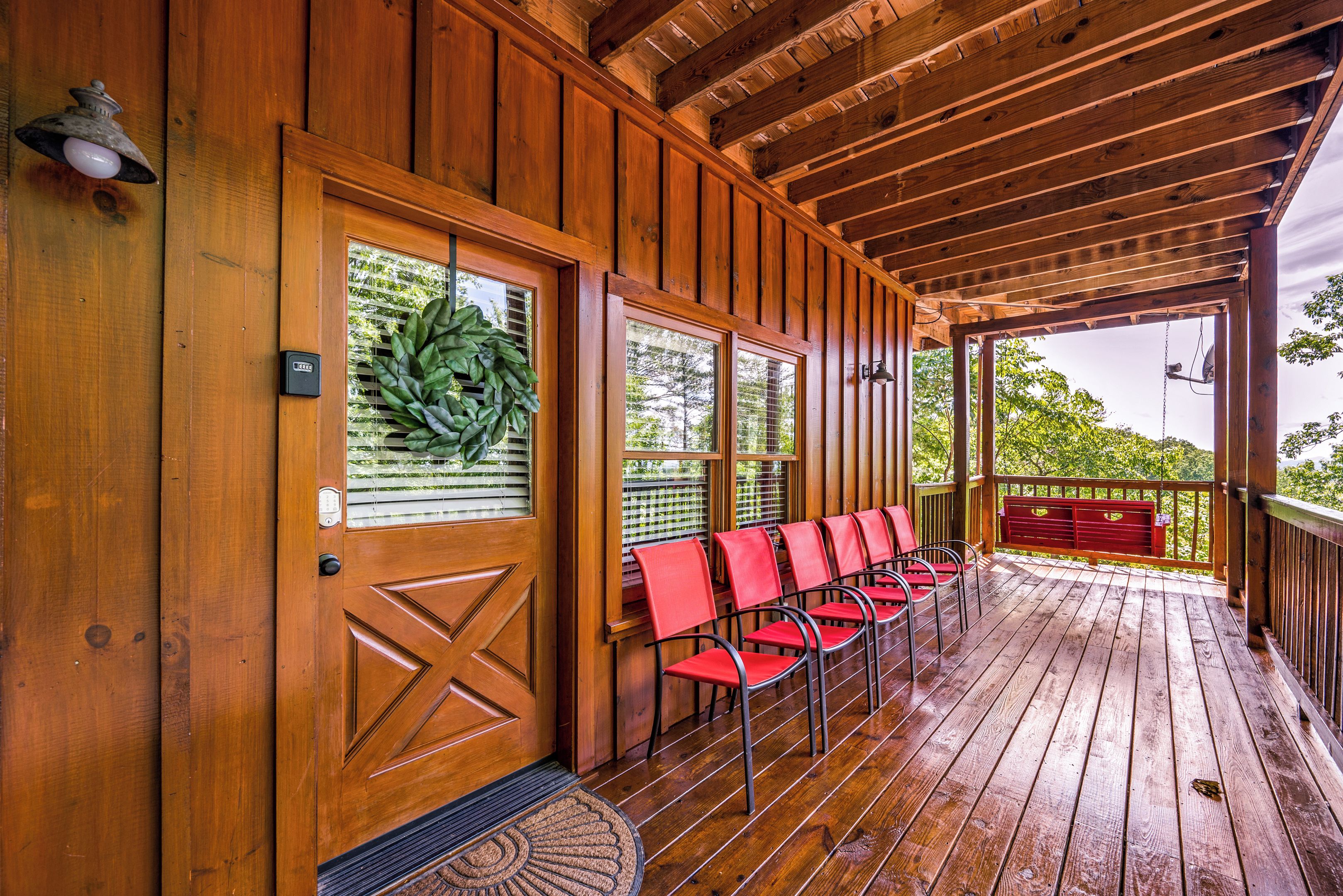 A wooden porch with a row of red chairs and a door with a wreath.
