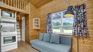 L’intérieur chaleureux d’un chalet comprend un coin cuisine, un canapé, une fenêtre avec des rideaux et un plafond en bois.