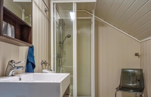 Une salle de bain avec un lavabo blanc, une douche en verre et une chaise noire.