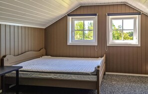 Une chambre avec un lit simple, deux fenêtres et un plafond en pente.