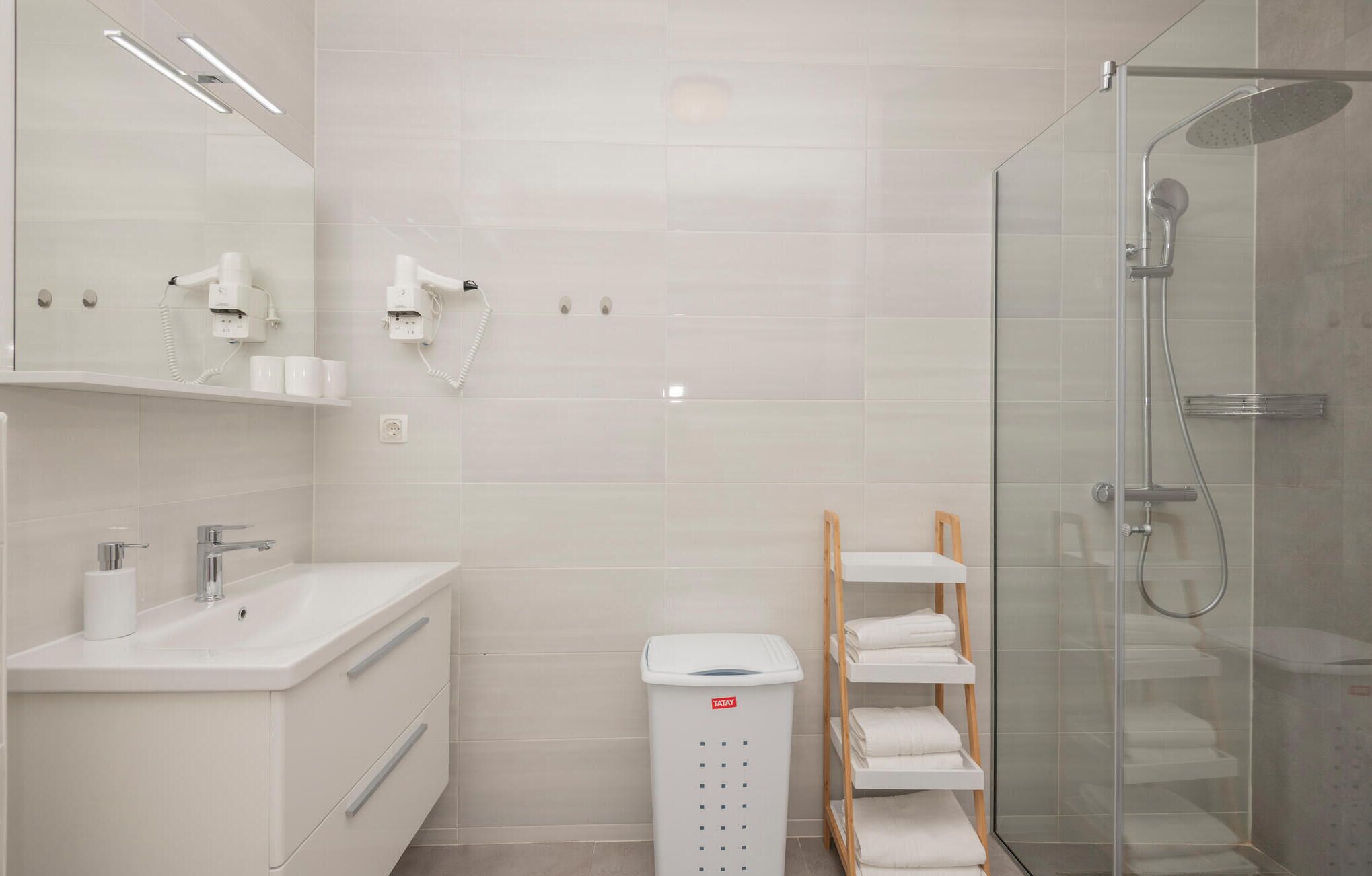 Un baño moderno con cabina de ducha de vidrio, un lavabo blanco y un cubo de basura TATAY.