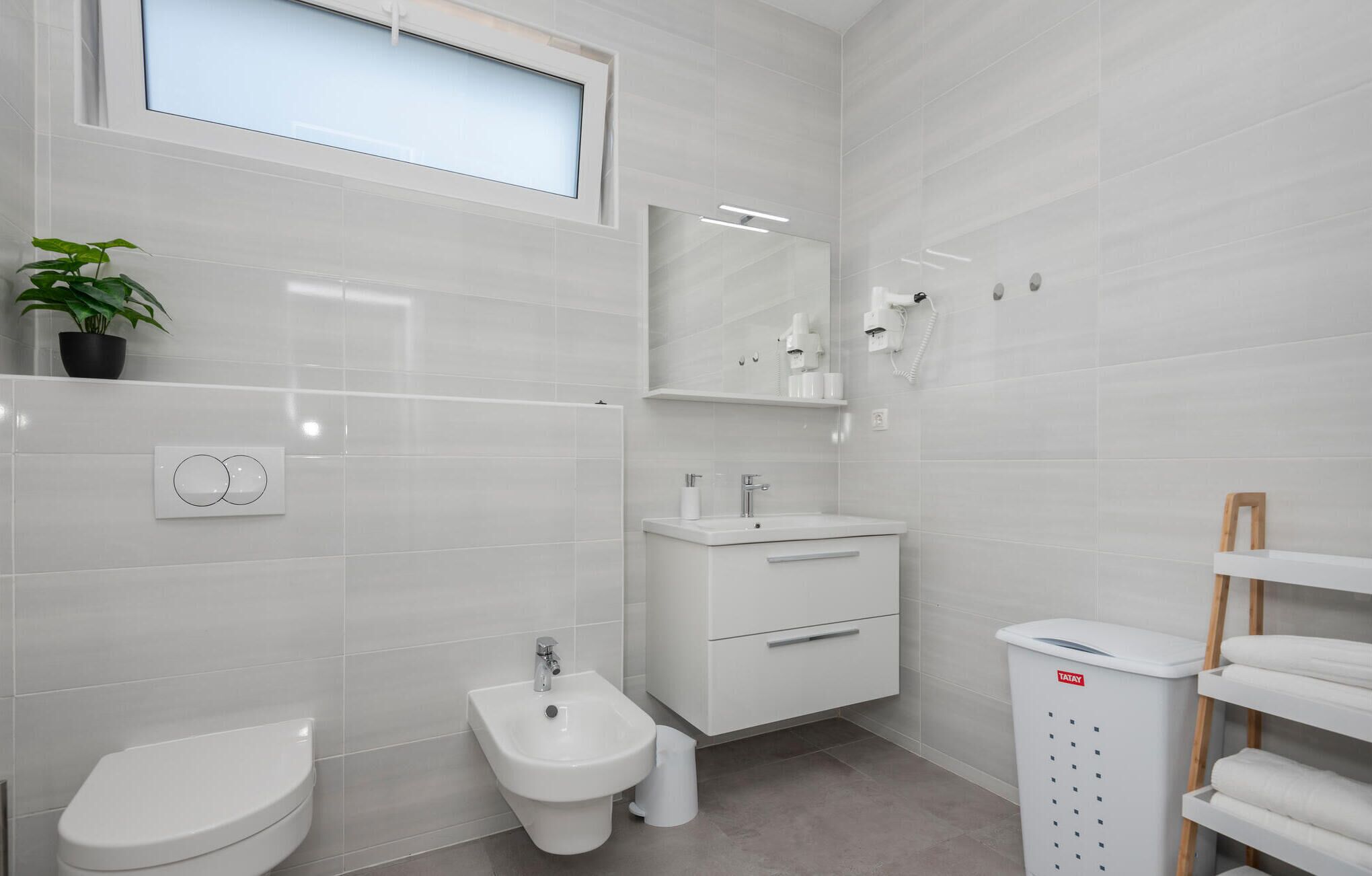 A modern bathroom with a toilet, bidet, vanity with a mirror, and a TATAY laundry basket.