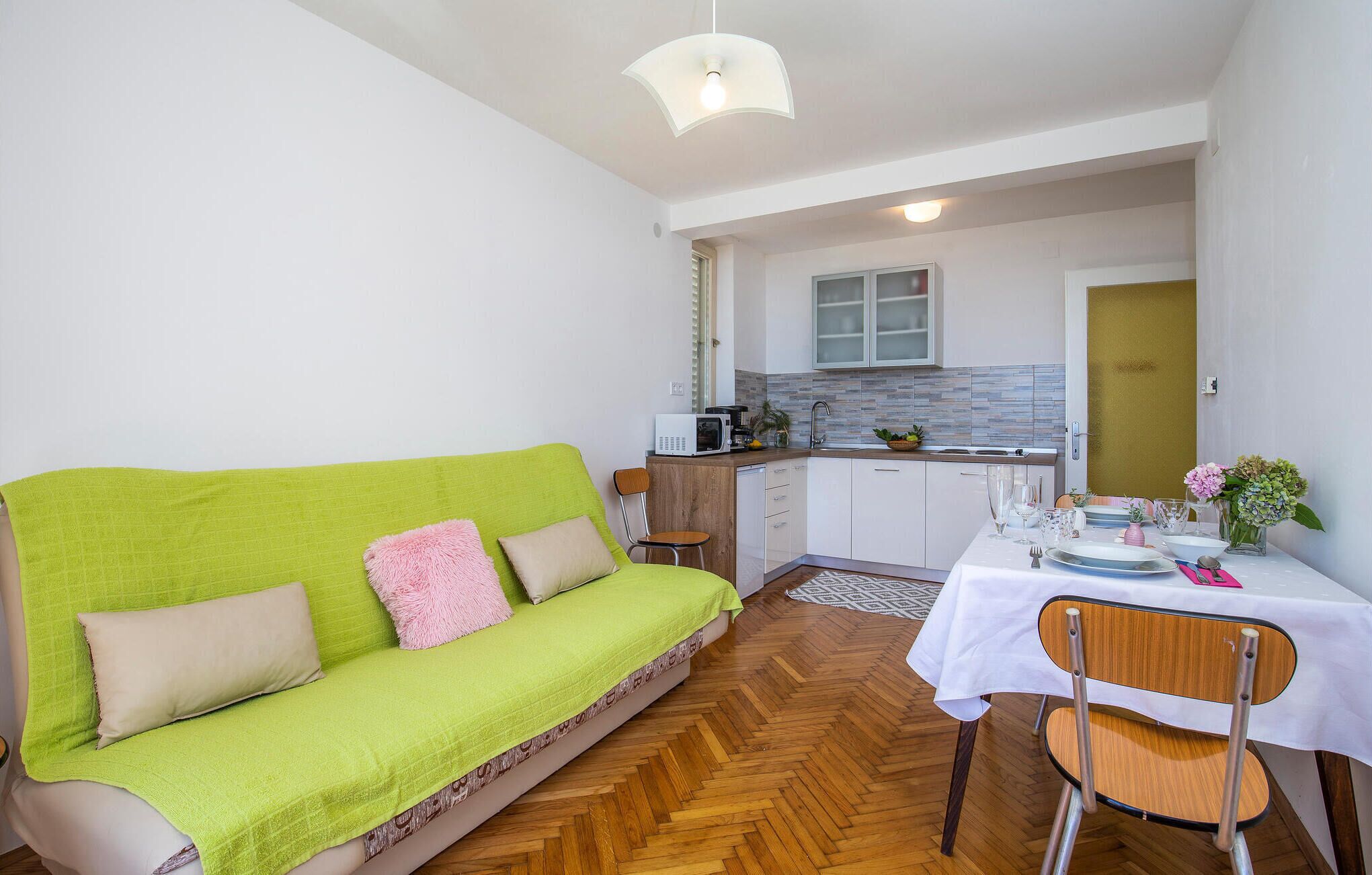 Un espace de vie compact comprenant un canapé vert, une table à manger pour deux personnes, un coin cuisine et un petit espace repas.
