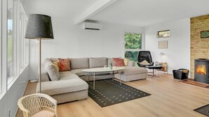 Ein modernes Wohnzimmer mit einer Eckcouch, einem runden Couchtisch, einem Kamin und einem großen Fenster mit Blick auf Grünflächen.