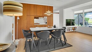 Eine moderne Küche mit Holzschränken, einem Esstisch mit vier Stühlen und einem großen Fenster mit Blick auf Grünflächen.