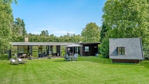Ein modernes Haus mit einer gläsernen Veranda, einer separaten Holzhütte und einem gepflegten Rasen.
