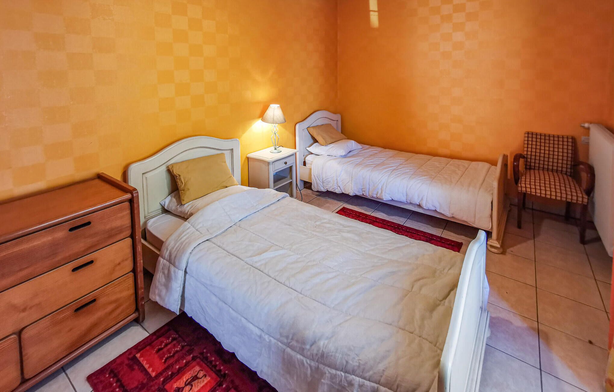 A bedroom with two single beds, a wooden dresser, a chair, and a nightstand with a lamp.