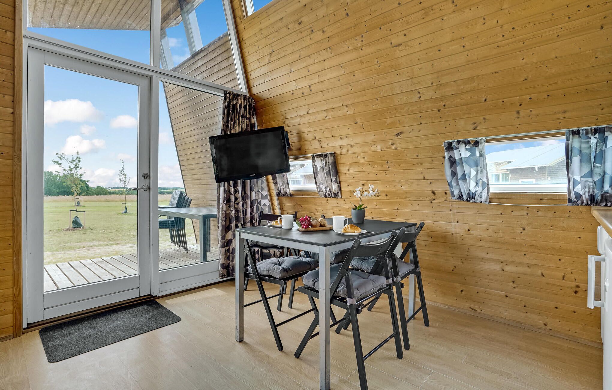 Une pièce chaleureuse au décor intérieur en bois, avec une table à manger et des chaises, un téléviseur à écran plat et une vue sur l’extérieur grâce à de grandes fenêtres.