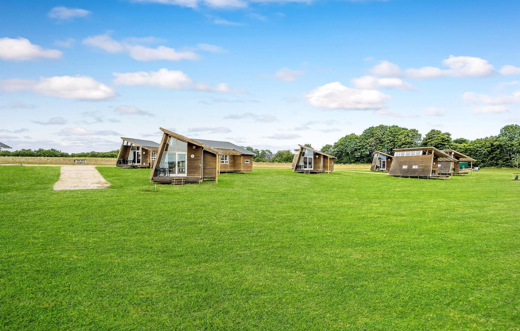 A series of wooden cabins in a grassy field with a clear sky.