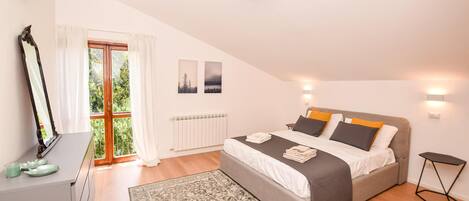 A bedroom with a bed, a dresser, a mirror, a window with curtains, a radiator, and a wall-mounted light fixture.