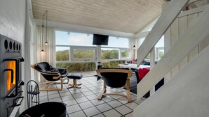 A cozy room with a fireplace, a TV mounted on the wall, and a view of the outdoors. - 4 bedroom stunning home in Hirtshals (Hirtshals)