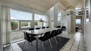 A modern dining area with a large table and chairs, large windows, and a staircase. - 4 bedroom stunning home in Hirtshals (Hirtshals)
