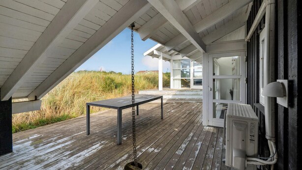A wooden deck with a swing, a white building with large windows, and a view of the beach. - 4 bedroom stunning home in Hirtshals (Hirtshals)