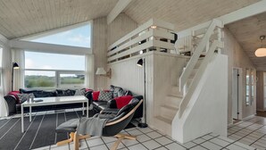 A spacious living area with a sofa, a chair, a table, and a staircase leading to an upper level. - 4 bedroom stunning home in Hirtshals (Hirtshals)