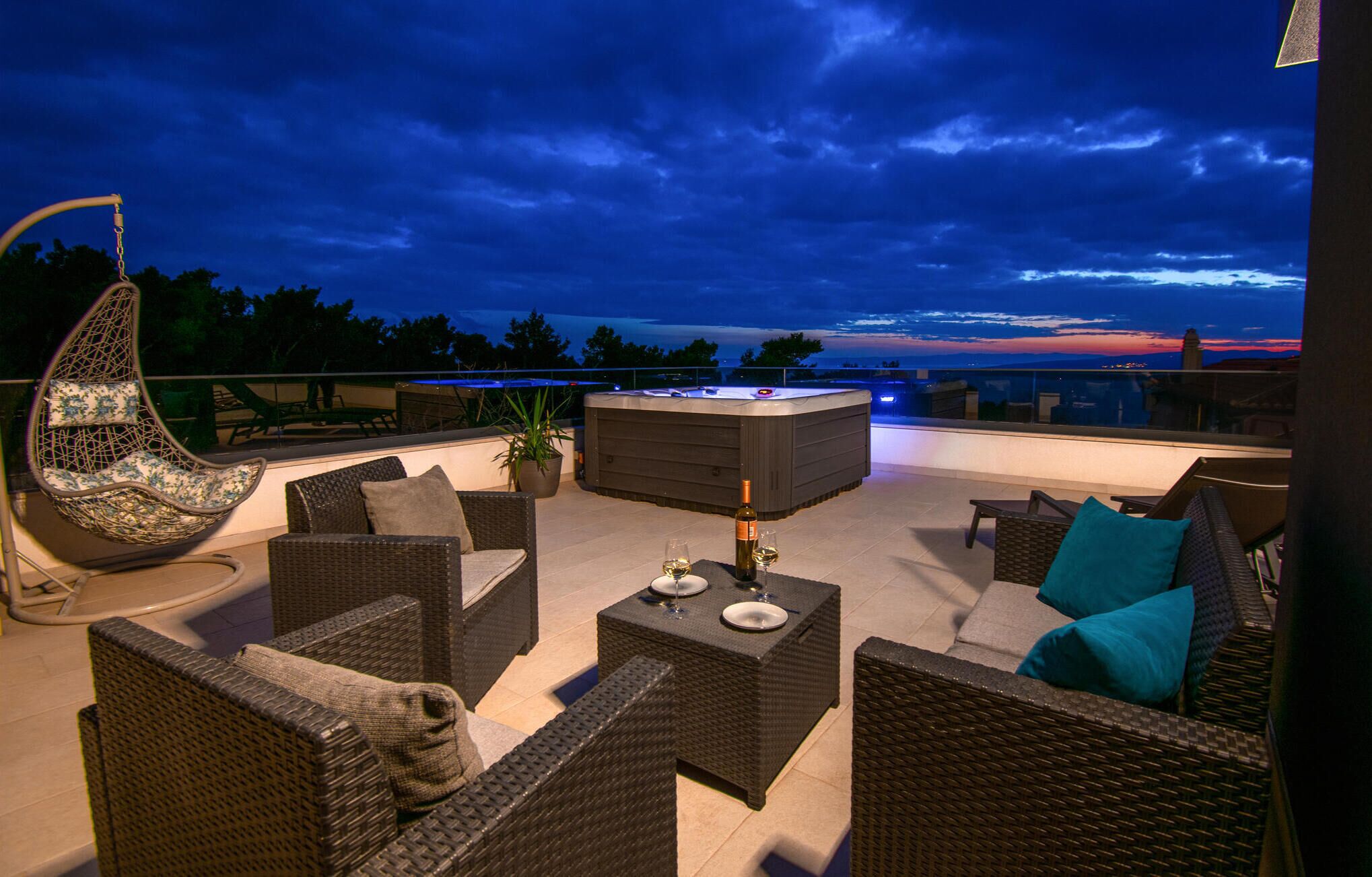 A rooftop terrace with wicker furniture, a hot tub, and a view of the sunset.