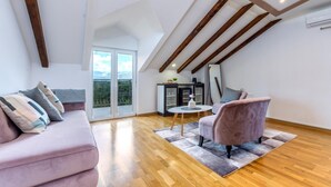 A spacious loft bedroom with a large window, wooden beams, a sofa, a chair, and a small table. - Amazing home in Vrlika with house a mountain view (Vrlika)