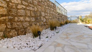 A stone pathway leading to a metal gate, flanked by white pebbles and decorative grasses. - Amazing home in Vrlika with house a mountain view (Vrlika)
