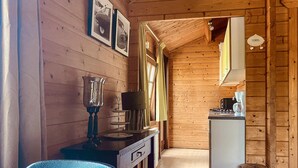 L’intérieur d’une cabane en bois comprend un coin cuisine, une table à manger avec des chaises et un petit réfrigérateur.