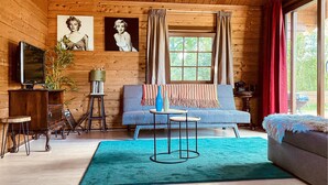 L'intérieur d'un chalet accueillant, avec un mur en bois, un canapé bleu, une petite table ronde et un téléviseur posé sur un meuble en bois.